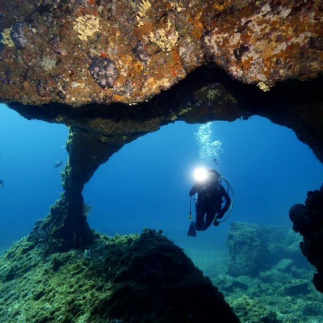 An underwater diver passing through a hole in the rock