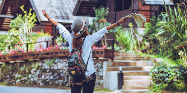 Freedom traveler woman standing with raised a book in hand arms and enjoying a beautiful nature. space for text.