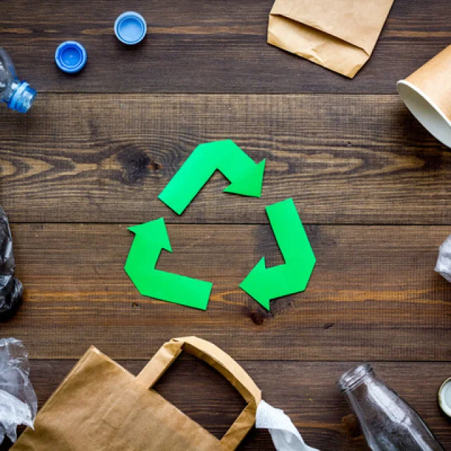 Green paper recycling sign among waste materials paper, plastic, polyethylene on dark wooden background top view