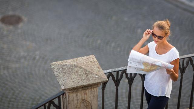 Pretty young female tourist studying a map, enjoying discovering a new city, looking excited (shallow DOF; color toned image)