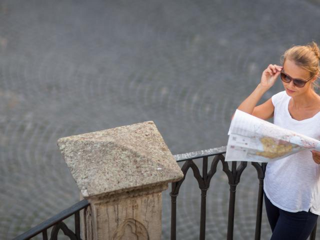 Pretty young female tourist studying a map, enjoying discovering a new city, looking excited (shallow DOF; color toned image)