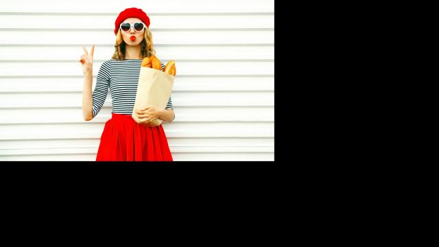 Portrait pretty cool girl wearing french red beret holding paper bag with long white bread baguette on white wall background