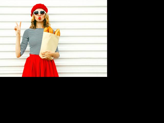 Portrait pretty cool girl wearing french red beret holding paper bag with long white bread baguette on white wall background