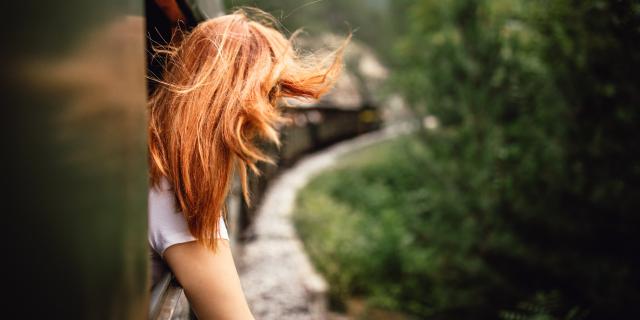 Happy smiling redhead woman looks out from window traveling by train