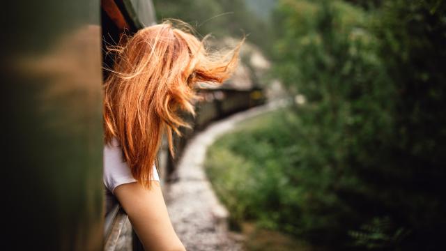 Happy smiling redhead woman looks out from window traveling by train