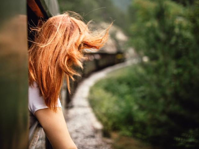 Happy smiling redhead woman looks out from window traveling by train