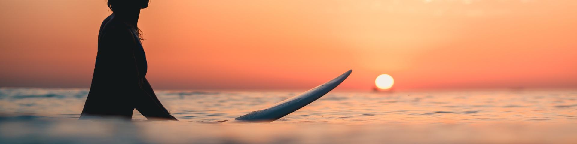 A surfer on the ocean with the breathtaking sunset in the sky in the background