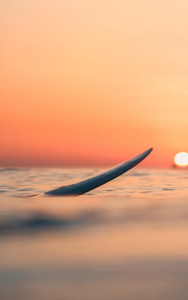 A surfer on the ocean with the breathtaking sunset in the sky in the background