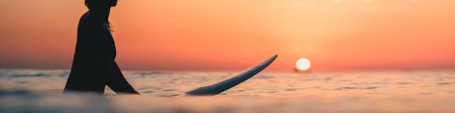 A surfer on the ocean with the breathtaking sunset in the sky in the background