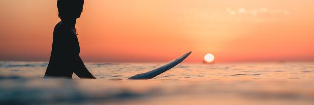 A surfer on the ocean with the breathtaking sunset in the sky in the background