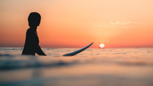 A surfer on the ocean with the breathtaking sunset in the sky in the background