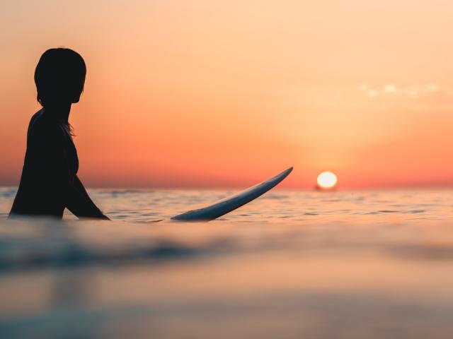 A surfer on the ocean with the breathtaking sunset in the sky in the background