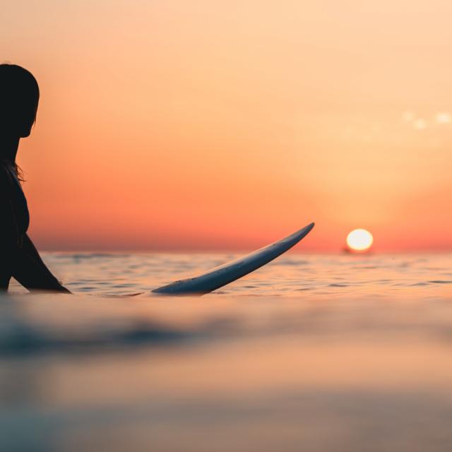 A surfer on the ocean with the breathtaking sunset in the sky in the background