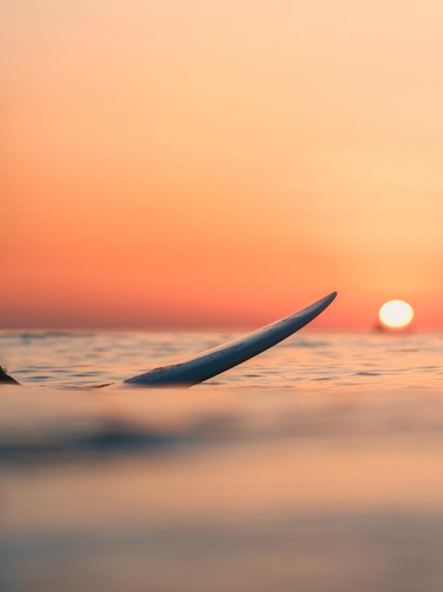 A surfer on the ocean with the breathtaking sunset in the sky in the background