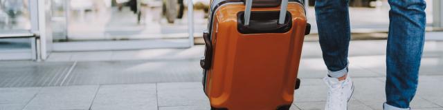 Close-up of man walking with suitcase. He is going in departure lounge. Copy space in left side