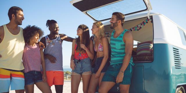 Group of friends interacting with each other near camper van at beach