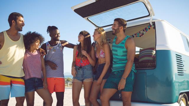 Group of friends interacting with each other near camper van at beach