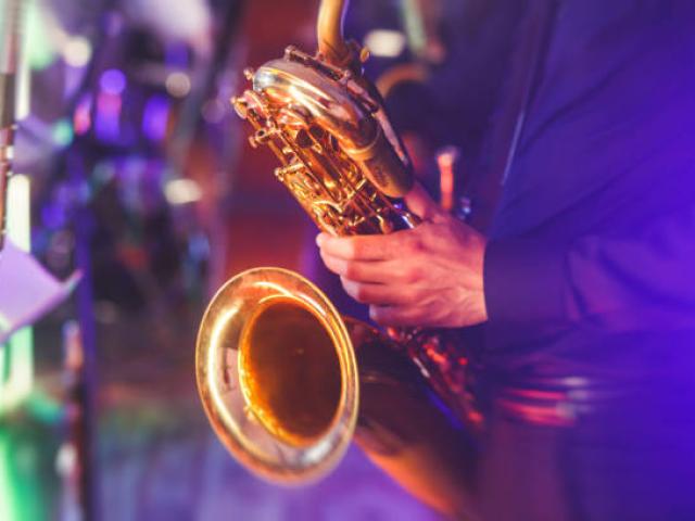 Concert view of a saxophone player with vocalist and musical jazz band in the background