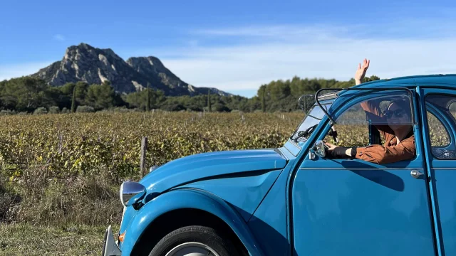 Une femme à bord d'une 2CV bleue devant un paysage de Provence