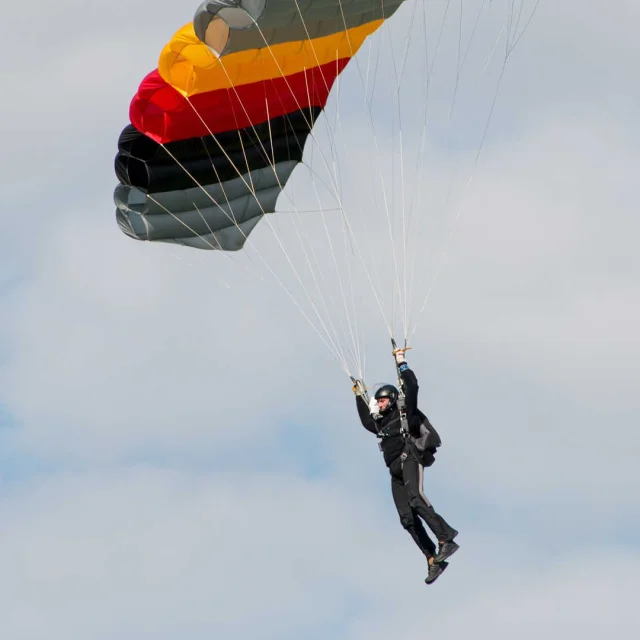 Homme qui vole dans le ciel avec un parachute aux couleurs du drapeau allemande