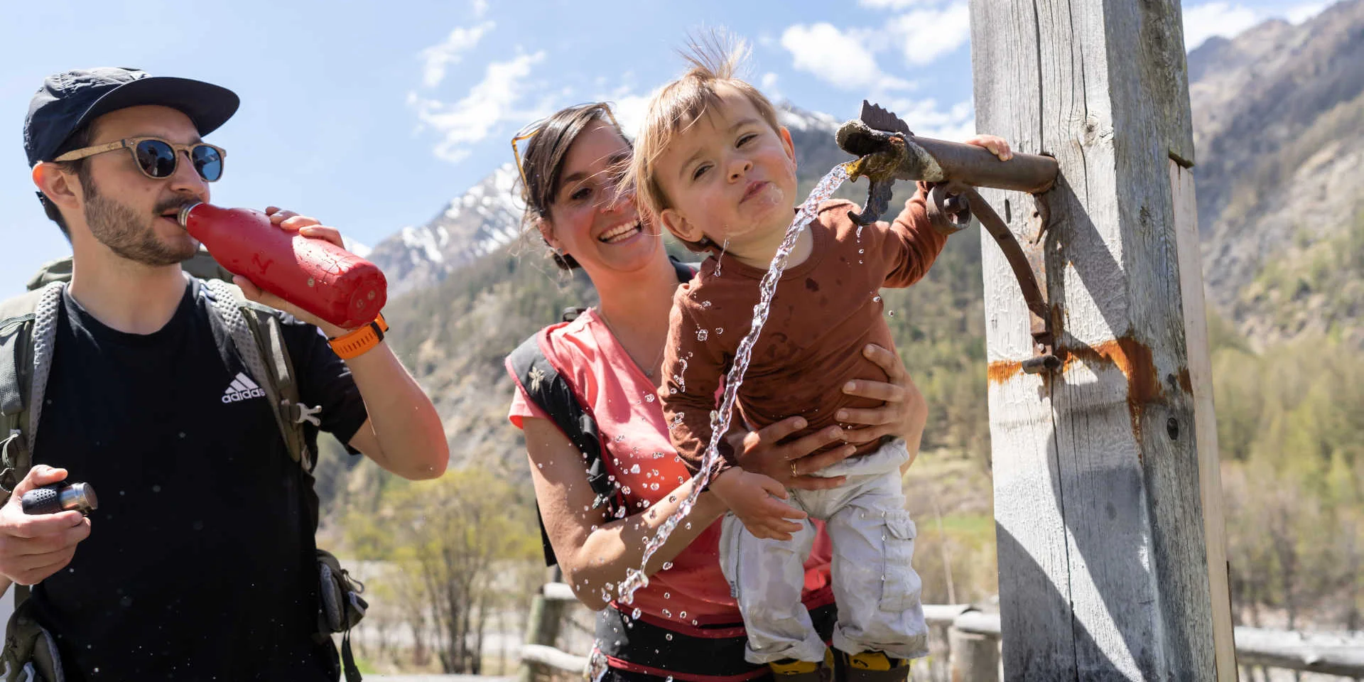 Couple and little boy drinking from a fountain in the Queyras mountains