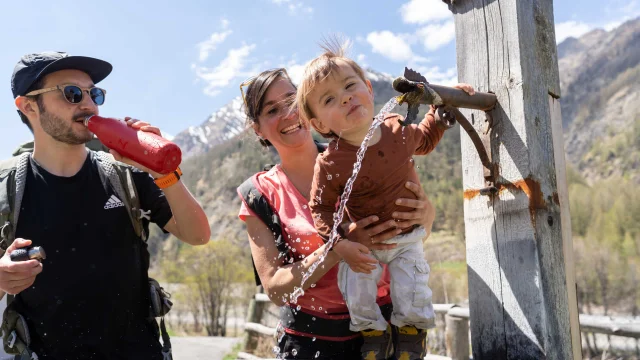 Paar und kleiner Junge trinken aus einem Brunnen in Queyras