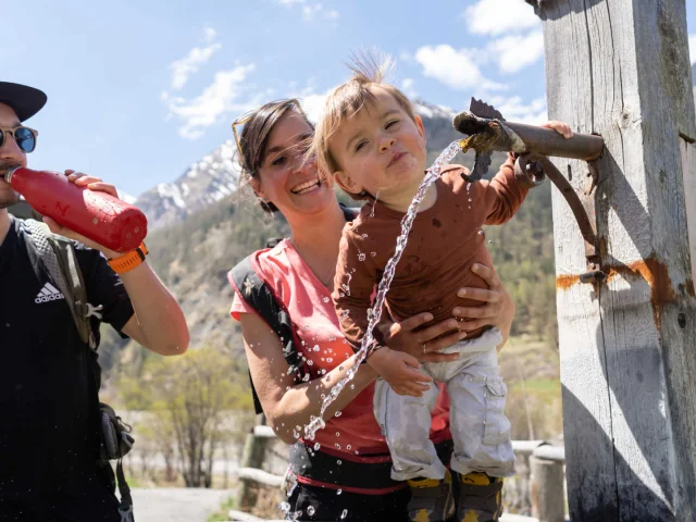 Couple and little boy drinking from a fountain in the Queyras mountains