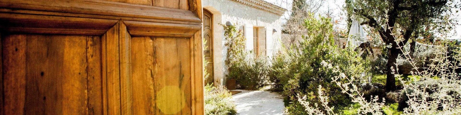 Une grande porte en bois qui s'ouvre sur l'entrée d'une bastide provençale et son jardin