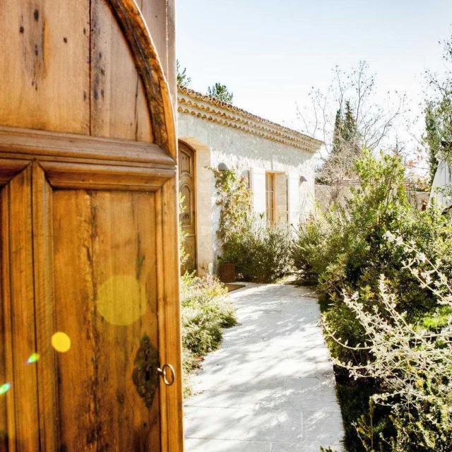 A large wooden door opening onto the entrance of a Provençal bastide and its garden