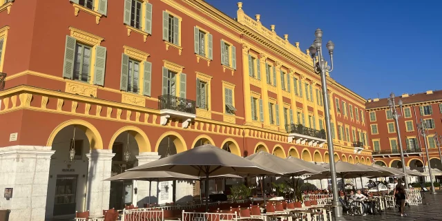 Une terrasse de café devant les immeubles oranges de la place Masséna à Nice