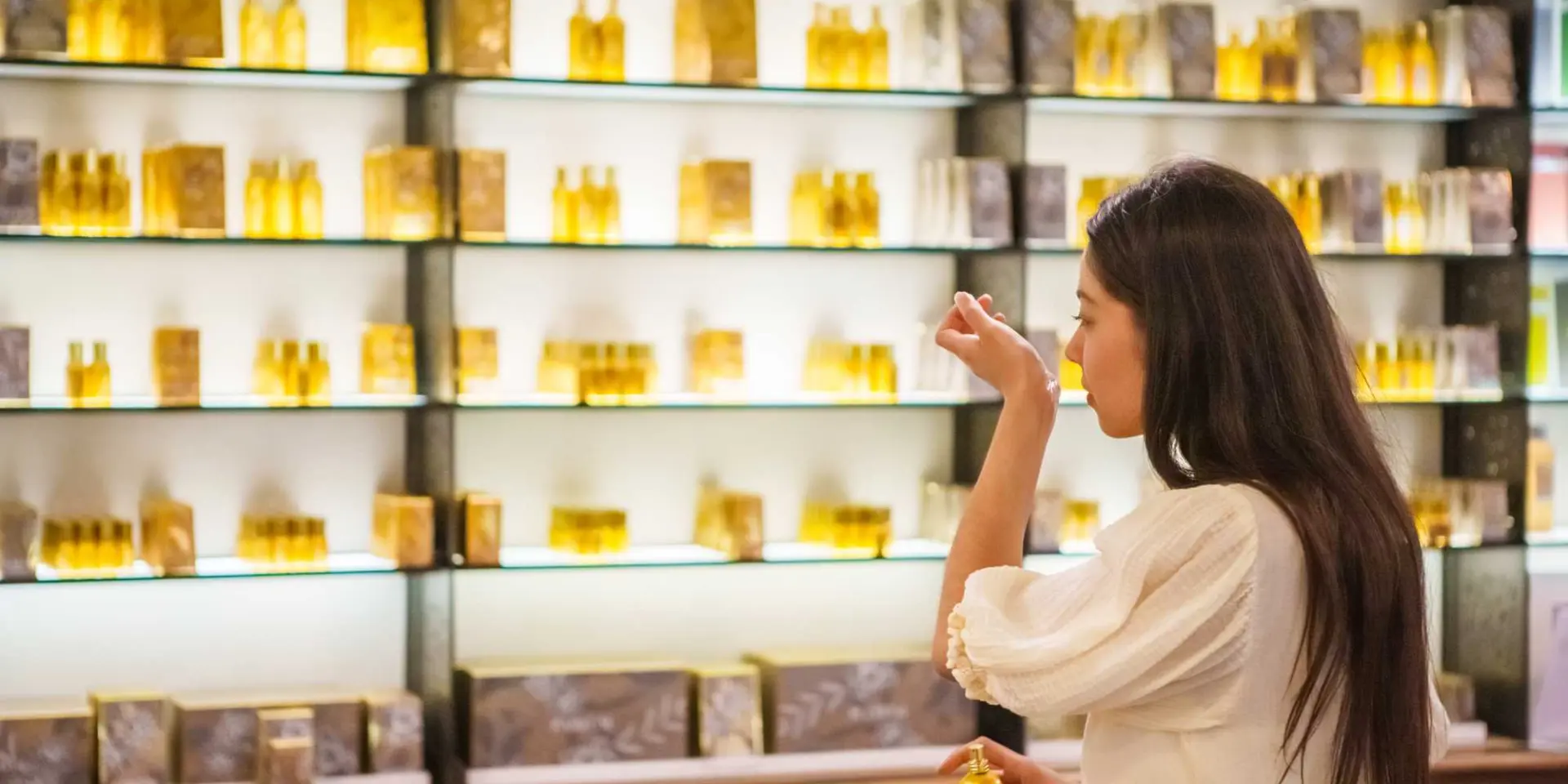 Interior of the Fragonard perfume museum and boutique, with illuminated shelves displaying rows of small golden glass bottles, and a visitor selecting a fragrance.
