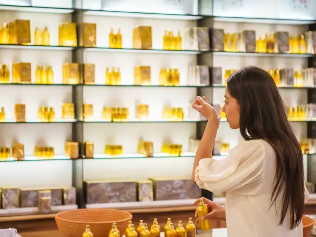 Interior of the Fragonard perfume museum and boutique, with illuminated shelves displaying rows of small golden glass bottles, and a visitor selecting a fragrance.
