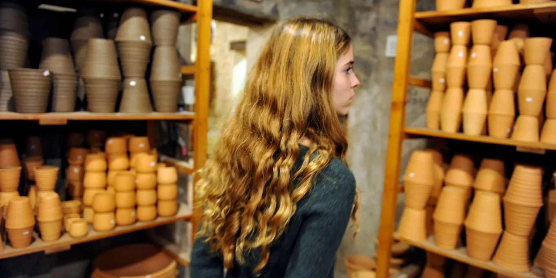 Interior of the Poterie Ravel workshop, with shelves filled with terracotta pots and bowls, and a visitor walking between rows of handcrafted ceramic pieces.