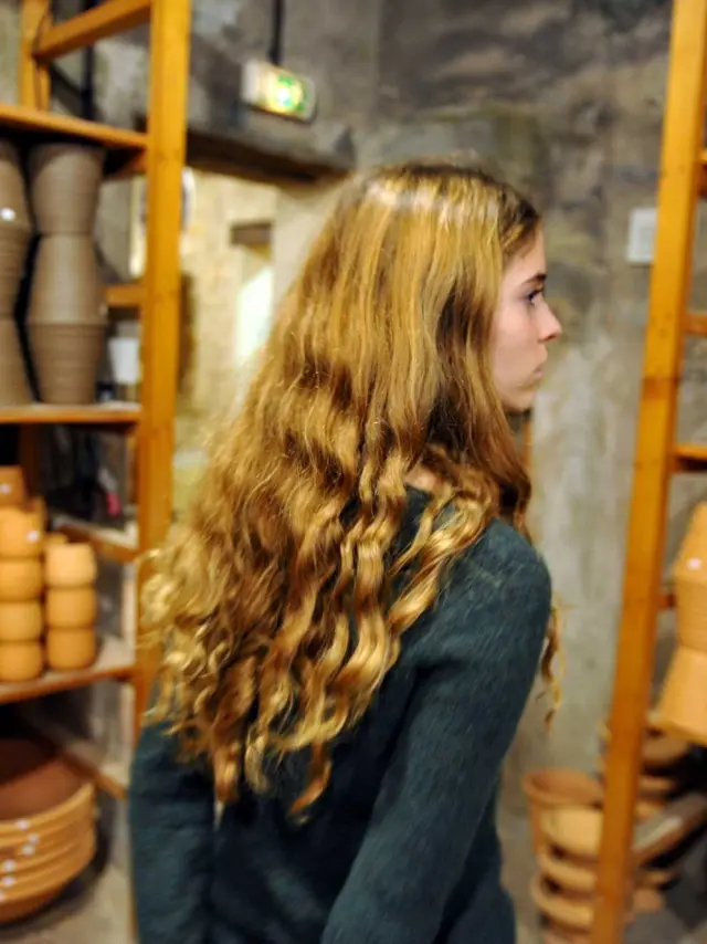 Interior of the Poterie Ravel workshop, with shelves filled with terracotta pots and bowls, and a visitor walking between rows of handcrafted ceramic pieces.