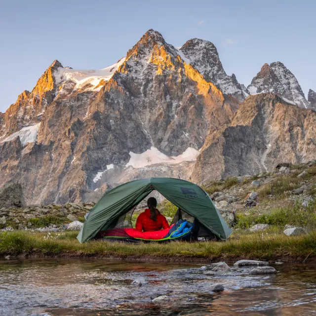 Une campeuse sous sa tente en bivouac au Tuckett, face aux sommets des Écrins